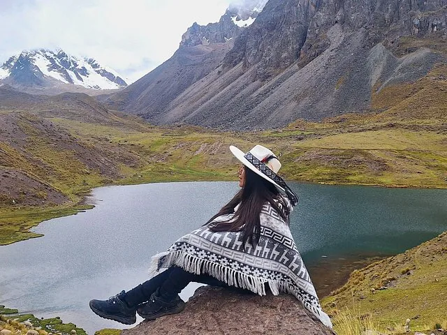 Woman sitting on a rock in a poncho looking at a lake