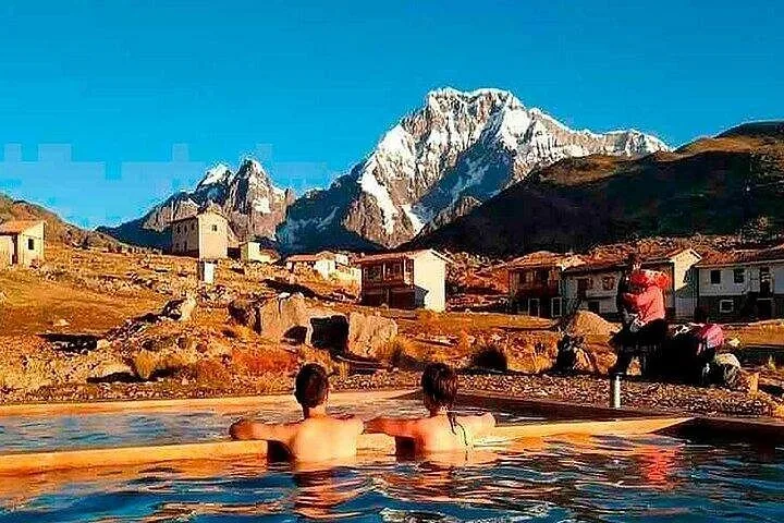Zwei Personen entspannen in einem Thermalbecken mit Bergen und Gebäuden im Hintergrund